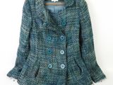 une veste en tweed bleu avec des boutons bleus, suspendue à un cintre sur un mur blanc
