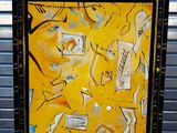 peinture abstraite jaune avec un cadre noir, posée sur un sol bleu, à côté d'un mur métallique