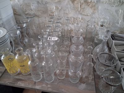 many empty glass bottles on a table with plates and cups