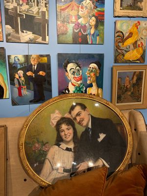 une photo représentant un homme et une femme assis sur une chaise devant un tableau représentant des clowns accroché au mur