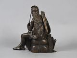 bronze statue of a man sitting on a rock with a rifle