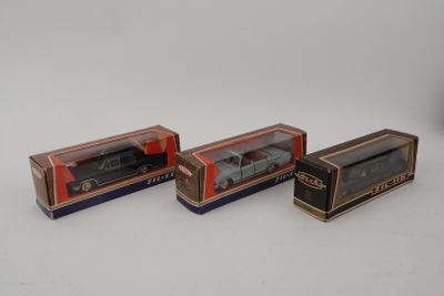 Trois petites voitures dans leur boîte sont alignées sur une surface blanche