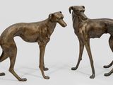 two bronze sculptures of greyhounds standing next to each other on a white surface
