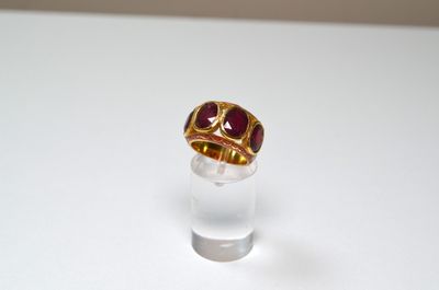 a gold ring with a red stone on top of a clear glass