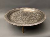 an ornate silver plate on a stand on a gray background