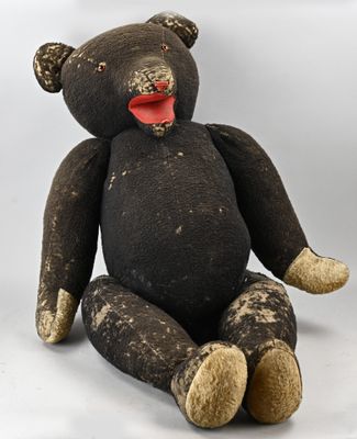 a black teddy bear sitting on the ground with a red tongue