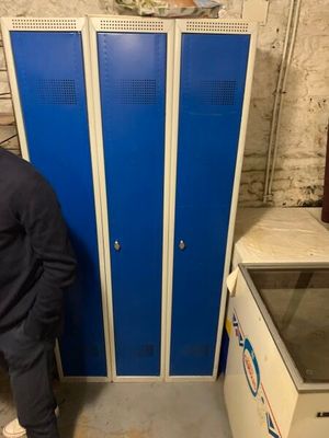 un homme debout à côté d'un casier bleu dans une pièce