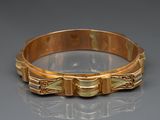 un gros plan d'un bracelet en or posé sur une surface réfléchissante