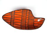 un plat en forme de poisson, orange et noir, posé sur un fond blanc