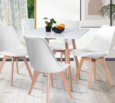 une table blanche avec quatre chaises et un bol de fruits posé dessus