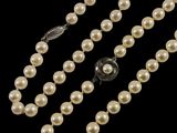 un collier de perles blanches muni d'un fermoir en argent, sur fond noir