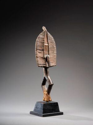 une sculpture représentant une personne tenant un objet en bois posé sur un socle noir