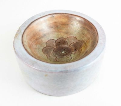 un petit bol orné d'une fleur, posé sur une surface blanche