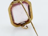a close up of a gold and pink glass broochle on a white surface