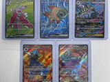 quatre cartes Pokémon différentes, rangées dans des pochettes en plastique, posées sur une table