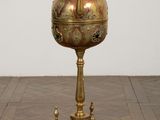 brass plated urn on stand on wooden floor with white wall in background