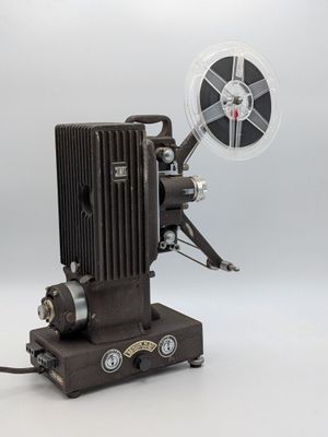 un vieux projecteur de cinéma posé sur une table, à côté d'une bobine