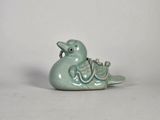 une petite figurine représentant un oiseau vert, posée sur une surface blanche