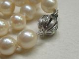 un collier de perles blanches muni d'un fermoir en argent, posé sur une table