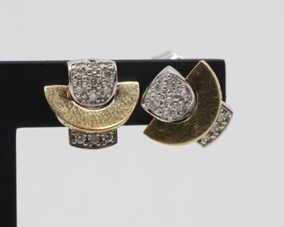 two gold and silver earrings with diamonds on a black stand