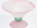 a pink glass bowl with a green base on a white surface
