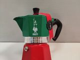 une cafetière rouge et verte posée sur une table blanche