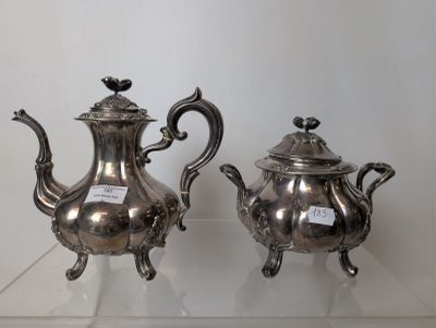 two silver teapots on display on a glass shelf