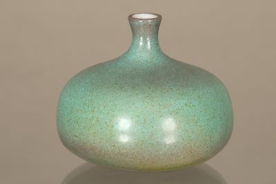 un vase vert posé sur une table, sur fond marron