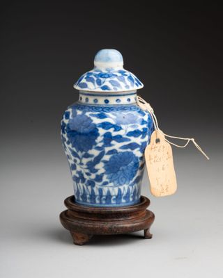 blue and white porcelain jar with lid on wooden stand with tag