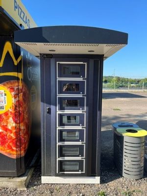 un distributeur automatique de pizzas et une poubelle dans un parking
