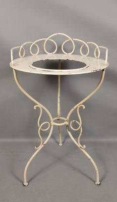 une table en fer forgé blanc avec un plateau en verre et un piètement en métal