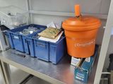 an orange bucket sitting on top of a metal shelf next to blue bins