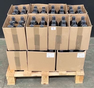 Des cartons de vin sont empilés sur une palette devant un mur noir