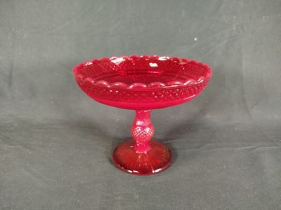 un bol en verre rouge posé sur un socle, sur fond gris