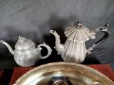 two silver teapots and a silver plate on a red place mat