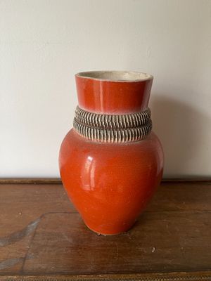 un vase rouge posé sur une table en bois, avec un mur blanc en arrière-plan