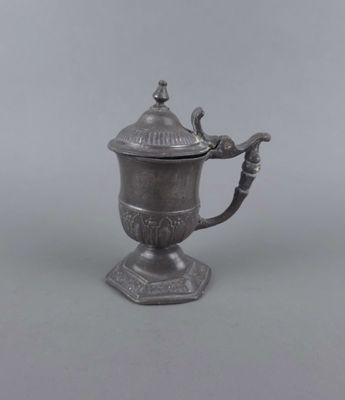 une cafetière ancienne en métal argenté, surmontée d'un oiseau