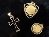 trois pendentifs en or représentant une croix et une médaille, sur un fond noir