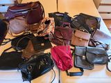 many different purses on a bed with a person standing next to them