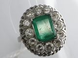a close up of a ring with a green stone surrounded by diamonds
