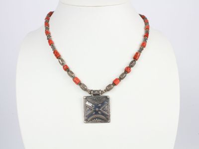 un collier avec un pendentif carré et des perles rouges sur un mannequin