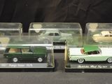 three green and white model cars in clear boxes on a black surface