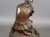 bronze statue of a man sitting on a rock with a hat on his head