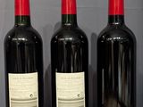 three bottles of wine sit on a wooden table next to a bottle of wine