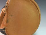 tan and black round purse with strap on a white surface