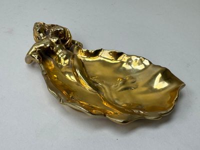 une assiette dorée ornée d'une feuille sur un fond blanc