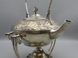 a silver teapot on a stand with a black handle