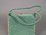 a green crocheted bag with a wooden handle on a gray background