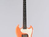 une guitare électrique orange accrochée à un mur blanc