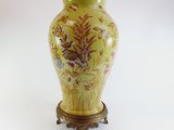 a yellow vase with flowers on it sitting on a stand